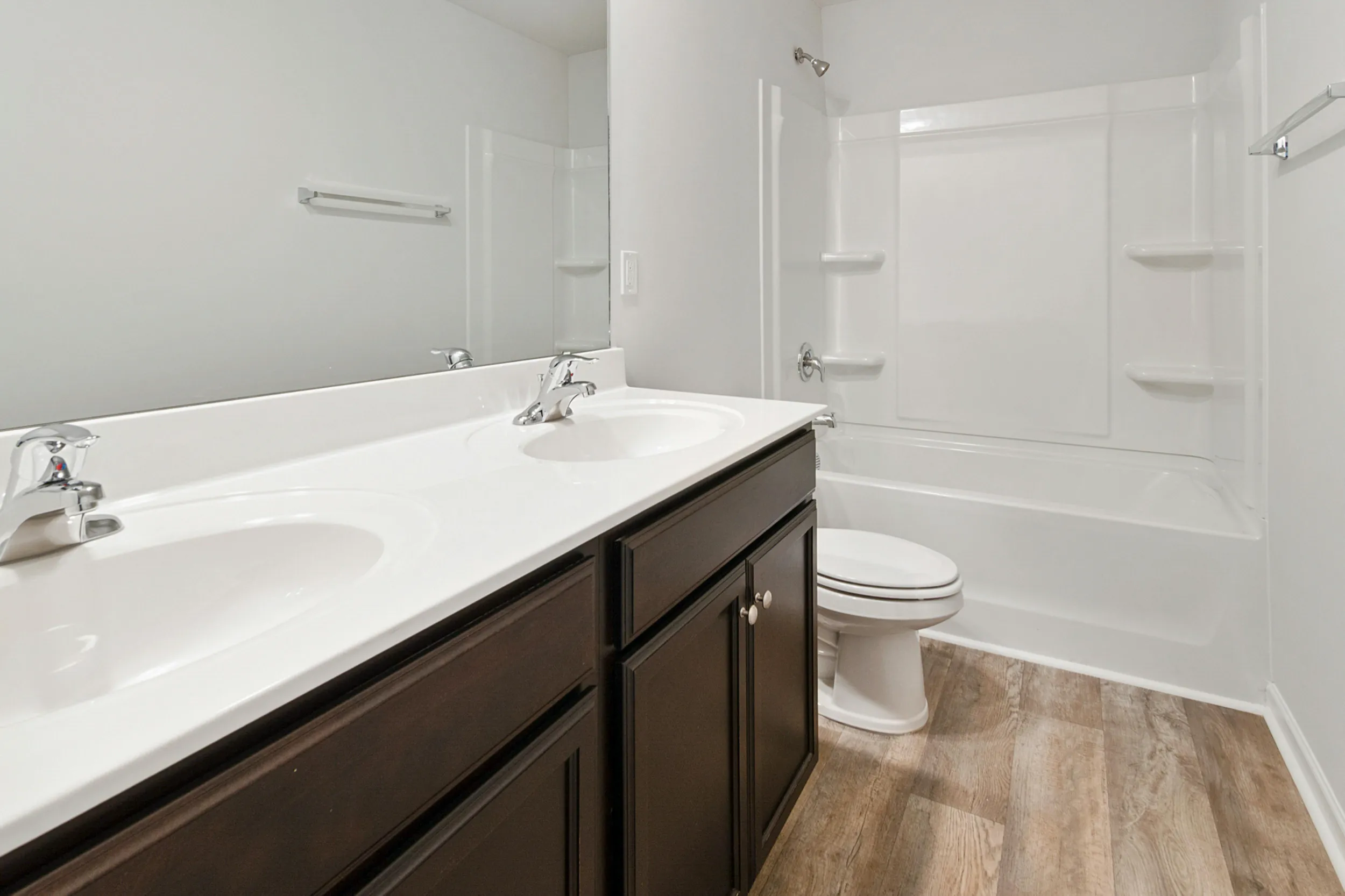 Modern badrumsinredning i Höllviken med mörk kommod, vita handfat och integrerad dusch.